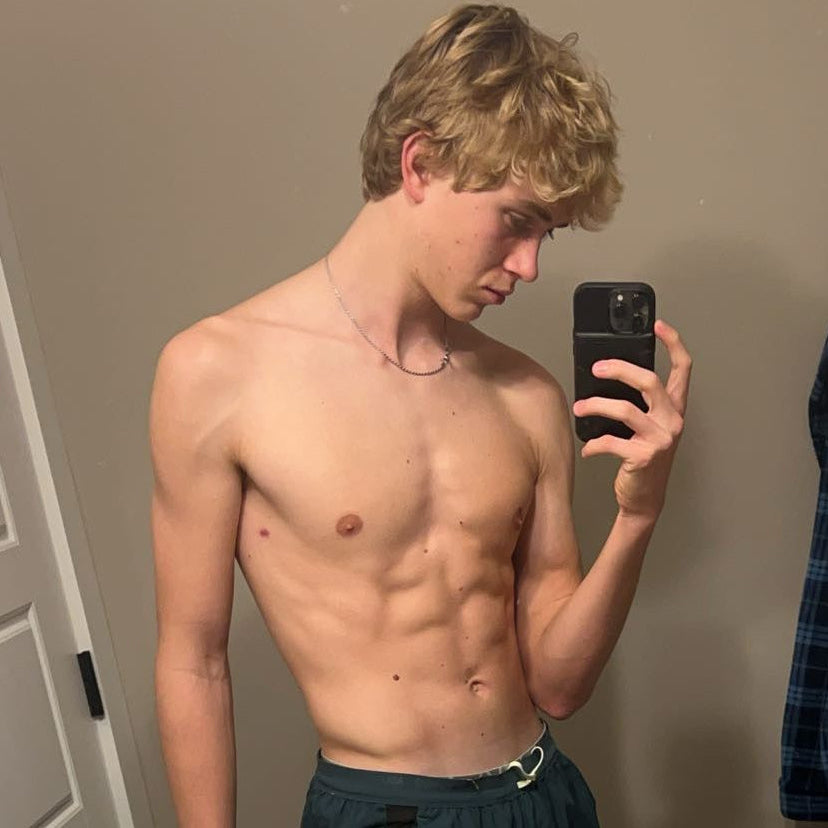 Man taking a mirror selfie without a shirt, holding a phone.